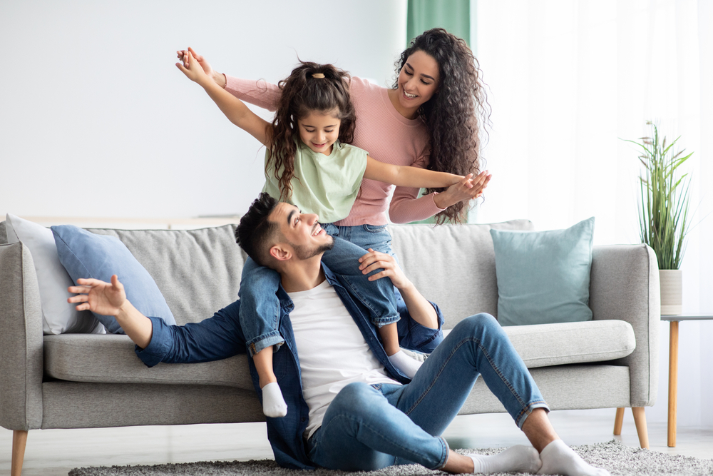 A couple sitting on a couch with a child in the air.