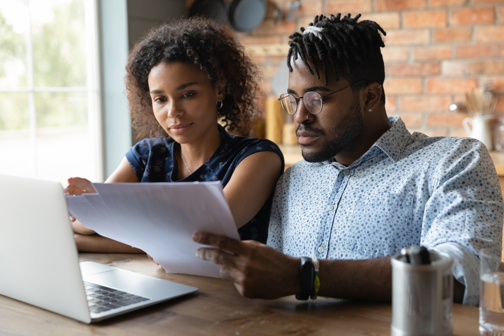 A couple looking at documents in front of a laptop.