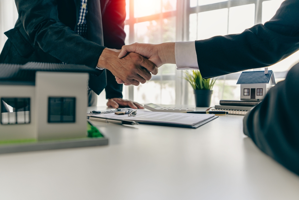 Two business people shaking hands over a house model.