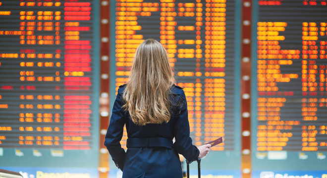 Flight delay compensation, woman stood in front of airport departures board showing delays and cancellations